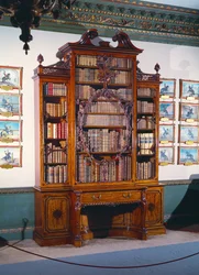 Bücherschrank mit Glasfront und großer zentraler Vitrine, dekoriert mit einem aufwendig geschnitzten inneren Rahmen, der eine geschnitzte Geige einbezieht, flankiert von zwei kürzeren schmalen Vitrinen, die auf einem unteren Abschnitt mit zwei Seitenschrän