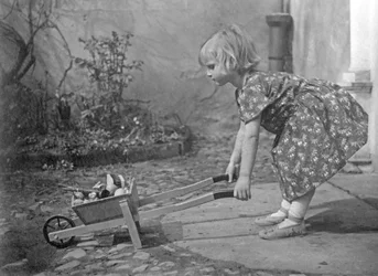 Kleines Mädchen spielt mit einer Schubkarre. Fotografie um 1931