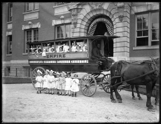 Kleine Mädchen posieren in und vor einem Pferdewagen, vor einem unbekannten Gebäude, wahrscheinlich das römisch-katholische Waisenhaus, Kingsbridge, Bronx, ca. 1910