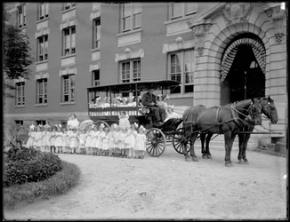 Kleine Mädchen posieren in und vor einem Pferdewagen, vor einem unbekannten Gebäude, wahrscheinlich das Römisch-Katholische Waisenhaus, Kingsbridge, Bronx, ca. 1910